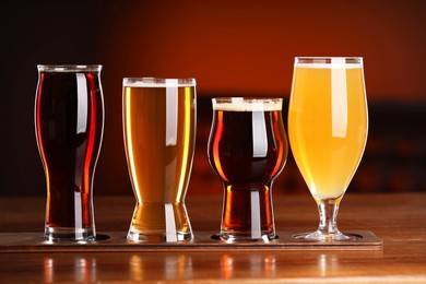 Photo of Glasses with different types of beer on wooden table against color background