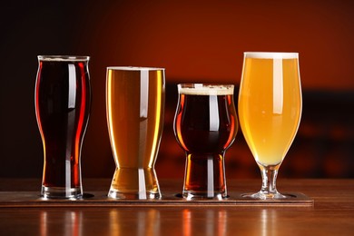 Photo of Glasses with different types of beer on wooden table against color background