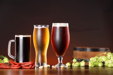 Photo of Glasses with different types of beer, snacks and fresh hops on wooden table in bar