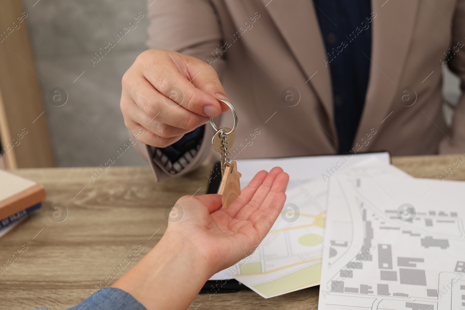 Photo of Real estate agent giving house key to new owner at wooden table, closeup