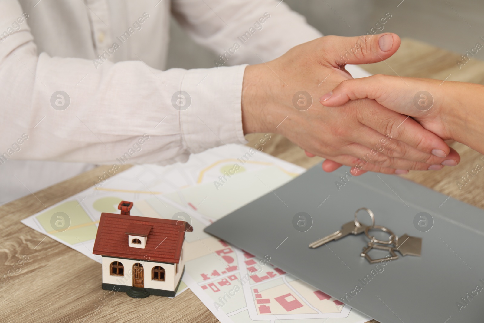 Photo of Real estate agent shaking hands with client at wooden table, closeup