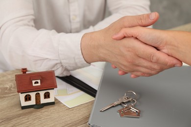 Photo of Real estate agent shaking hands with client at wooden table, closeup