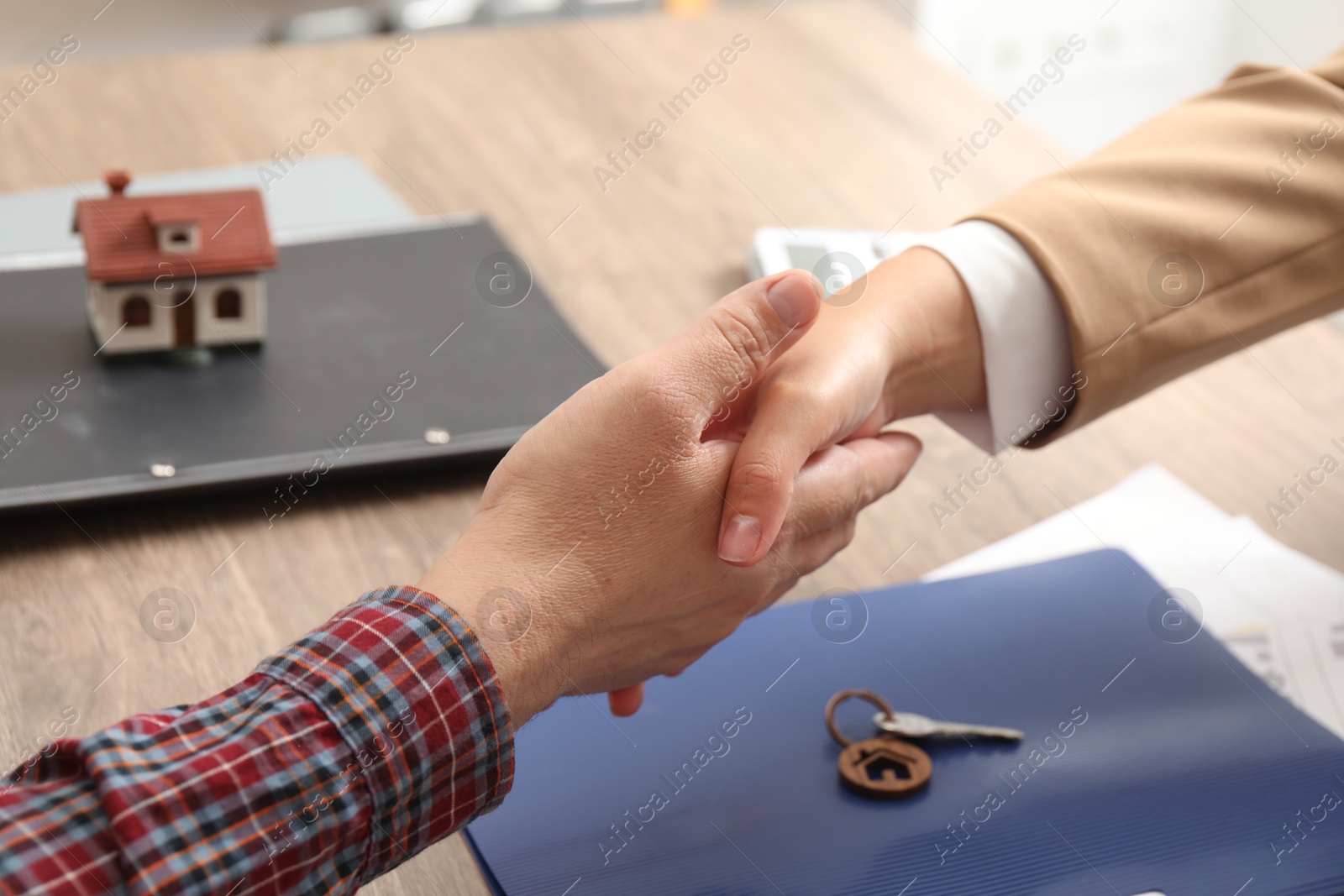 Photo of Real estate agent shaking hands with client at wooden table, closeup