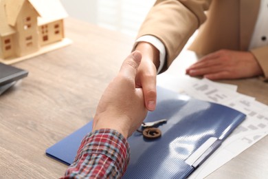 Photo of Real estate agent shaking hands with client at wooden table, closeup