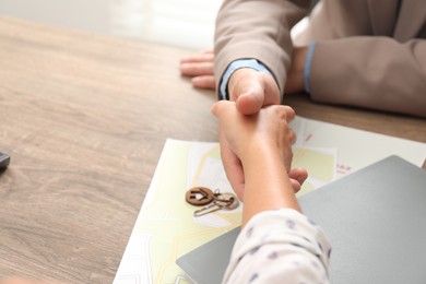 Real estate agent shaking hands with client at wooden table, closeup