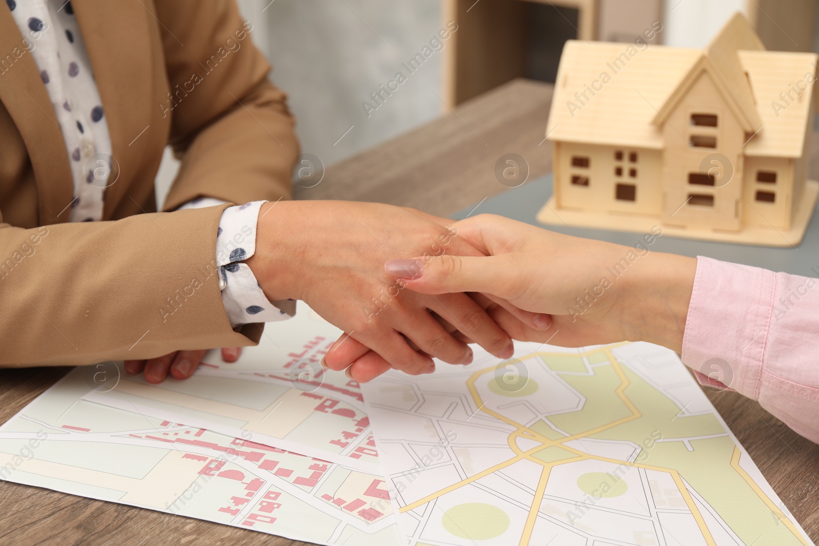 Photo of Real estate agent shaking hands with client at wooden table, closeup