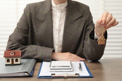 Real estate agent with house model, key and stationery at wooden table, closeup