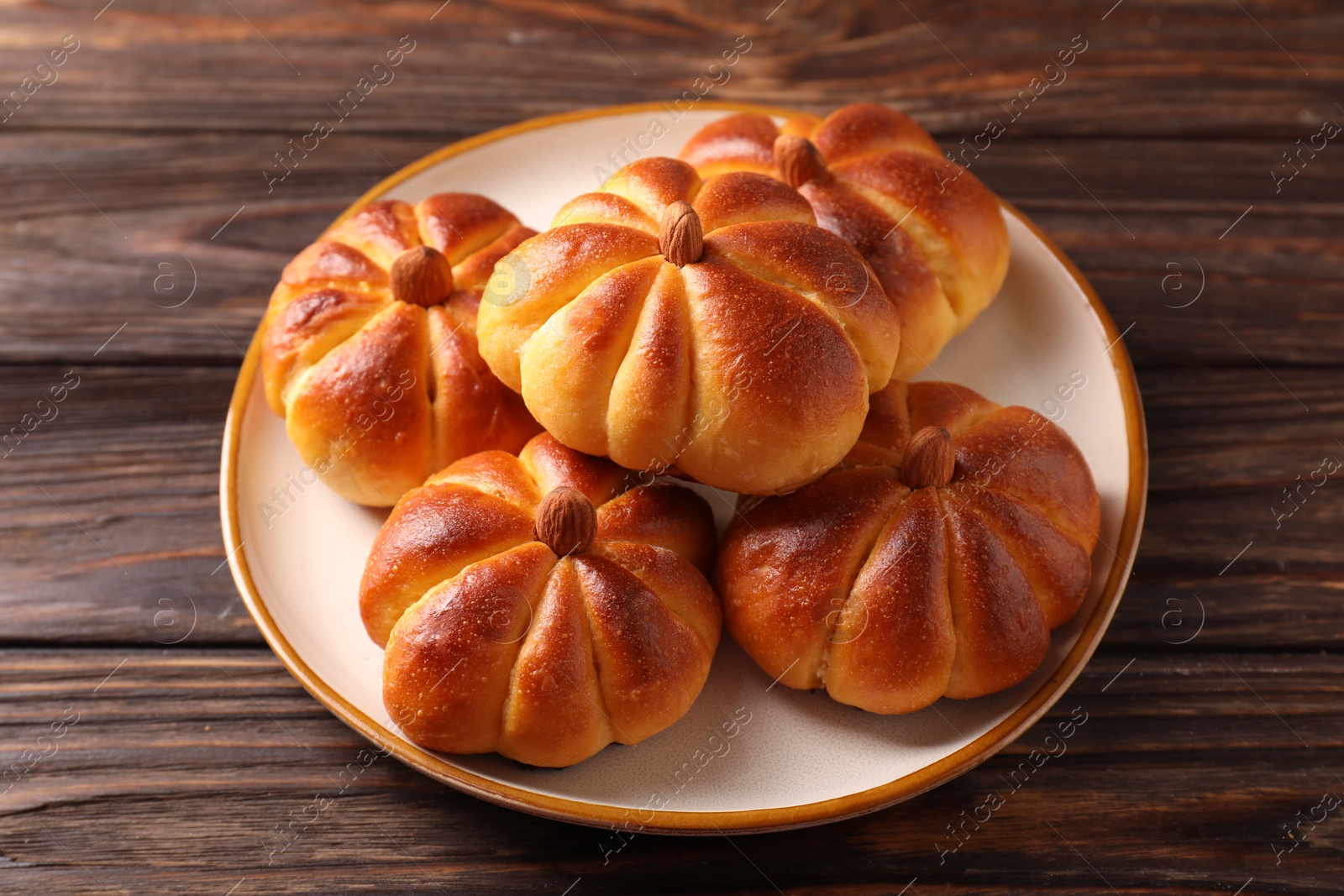 Photo of Tasty pumpkin shaped buns on wooden table, closeup