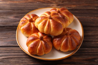 Photo of Tasty pumpkin shaped buns on wooden table, closeup