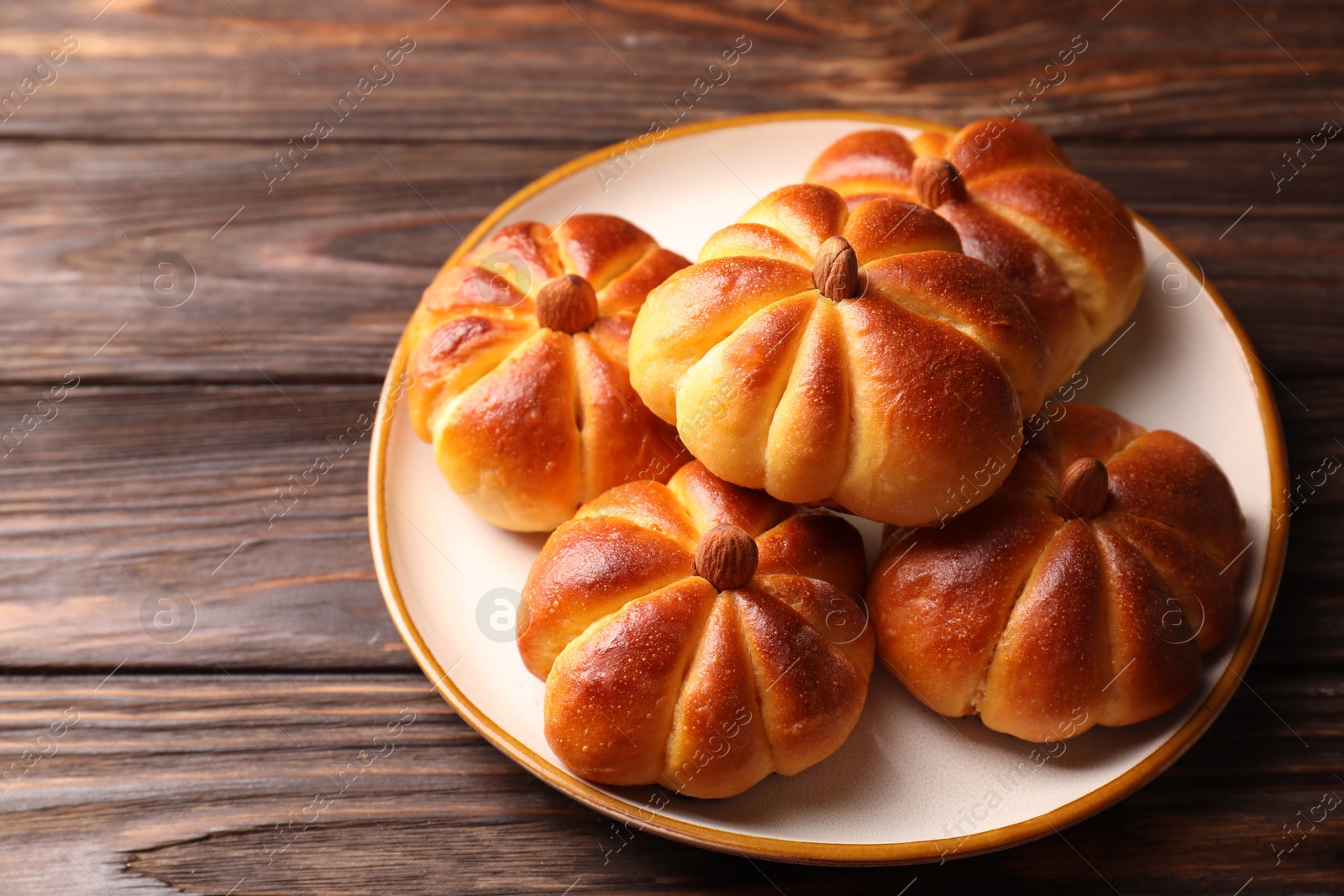 Photo of Tasty pumpkin shaped buns on wooden table, closeup