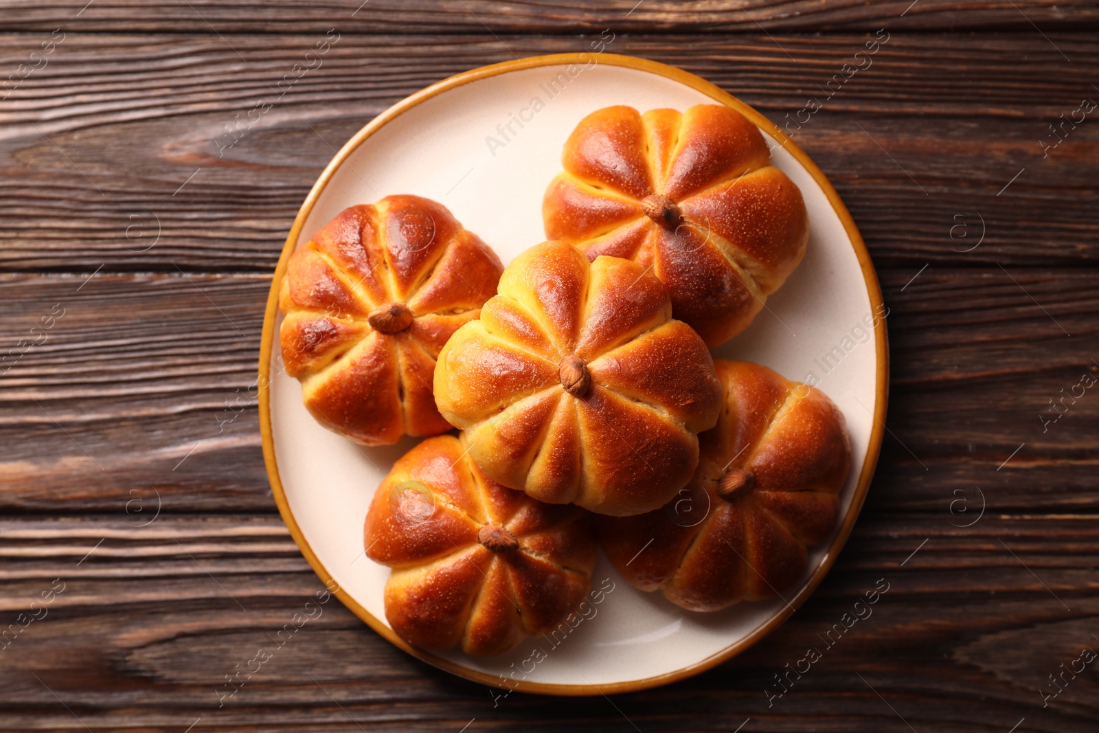 Photo of Tasty pumpkin shaped buns on wooden table, top view