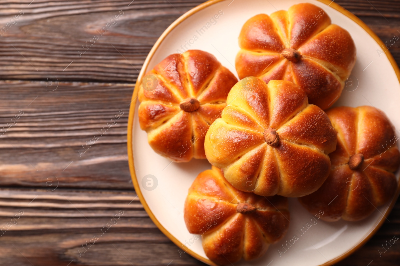 Photo of Tasty pumpkin shaped buns on wooden table, top view