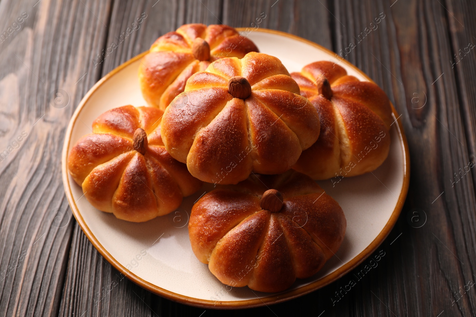 Photo of Tasty pumpkin shaped buns on wooden table, closeup