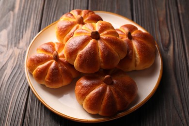 Photo of Tasty pumpkin shaped buns on wooden table, closeup