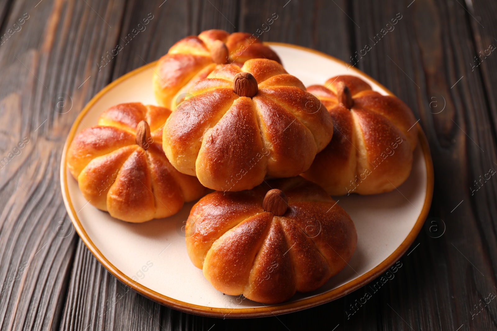 Photo of Tasty pumpkin shaped buns on wooden table, closeup