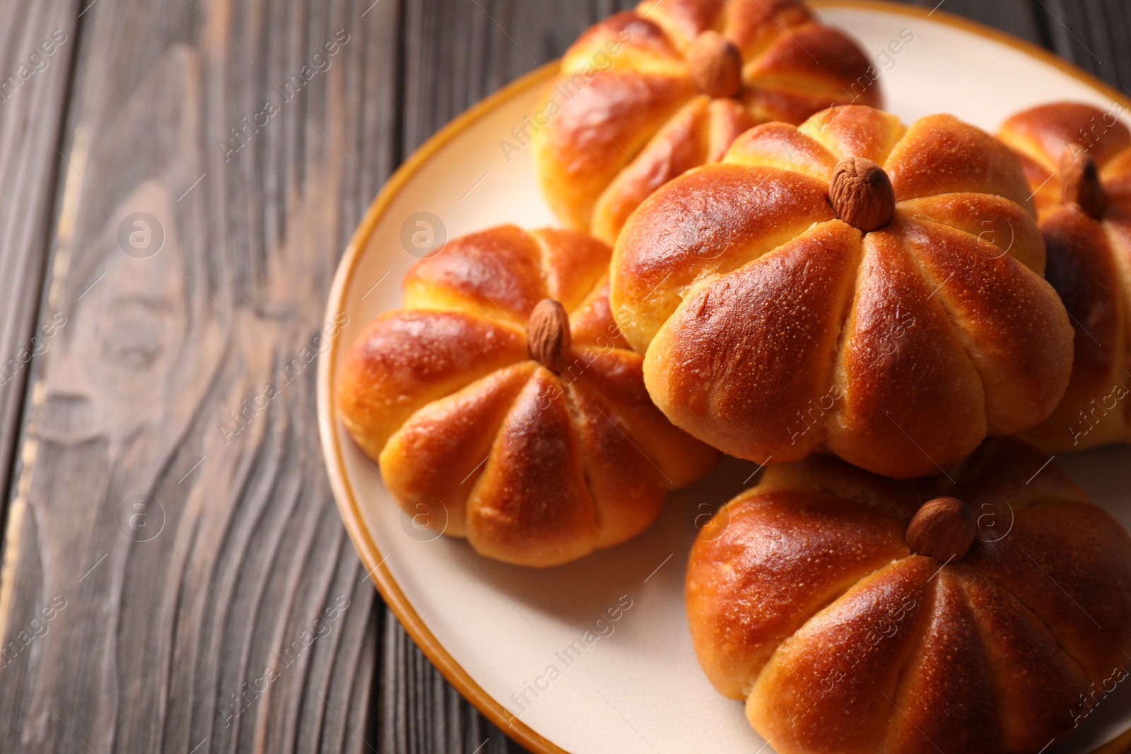 Photo of Tasty pumpkin shaped buns on wooden table, closeup