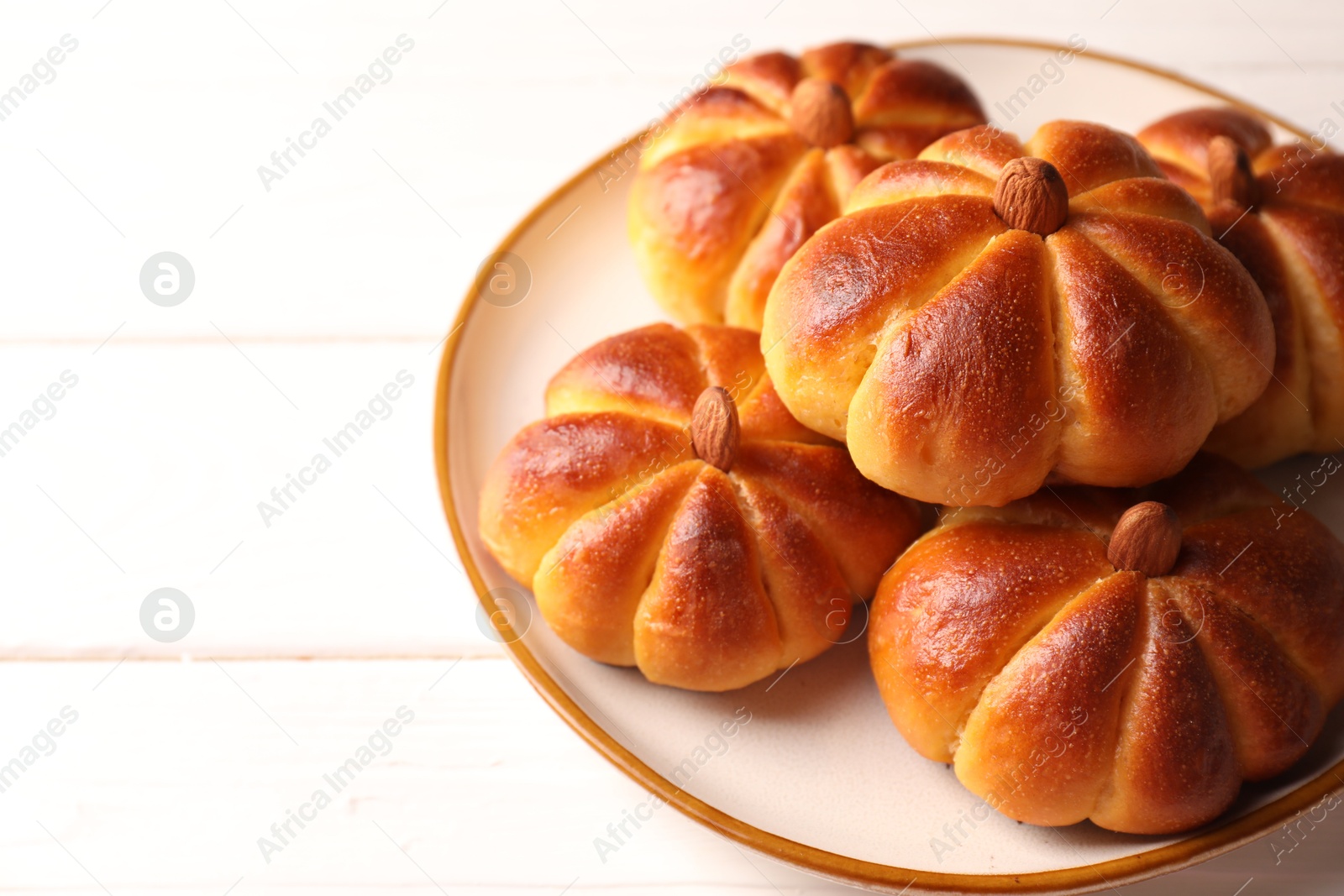 Photo of Tasty pumpkin shaped buns on white wooden table, closeup. Space for text