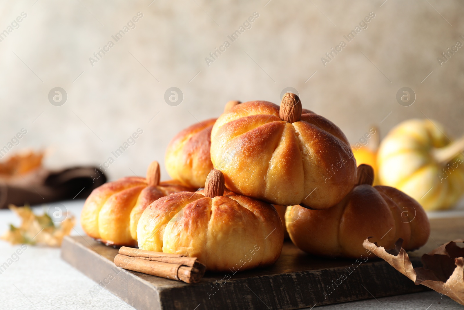 Photo of Tasty pumpkin shaped buns and cinnamon on light grey table, closeup