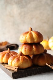 Photo of Tasty pumpkin shaped buns and cinnamon on light grey table, closeup