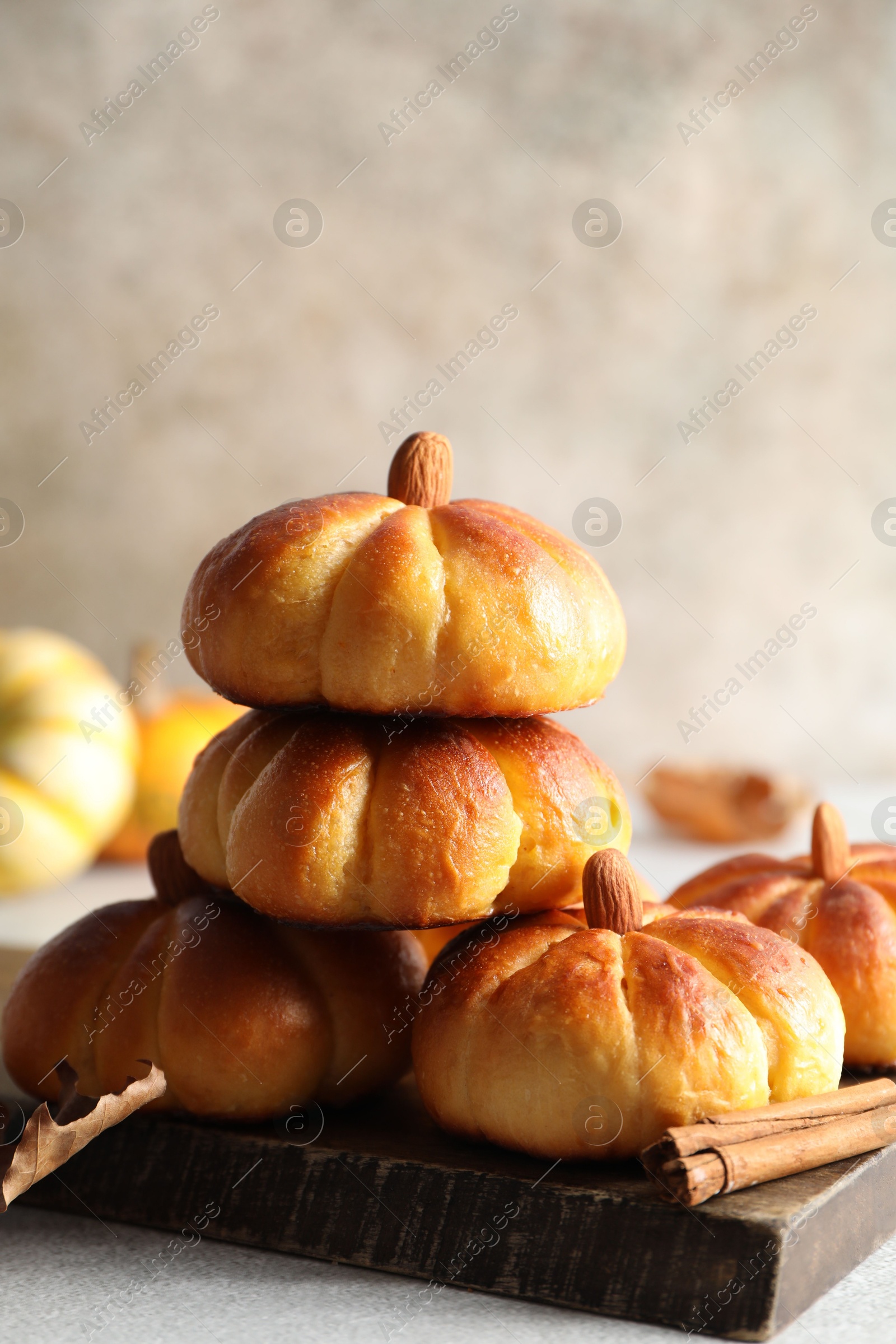 Photo of Tasty pumpkin shaped buns and cinnamon on light grey table, closeup