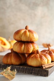 Photo of Tasty pumpkin shaped buns and cinnamon on light grey table, closeup