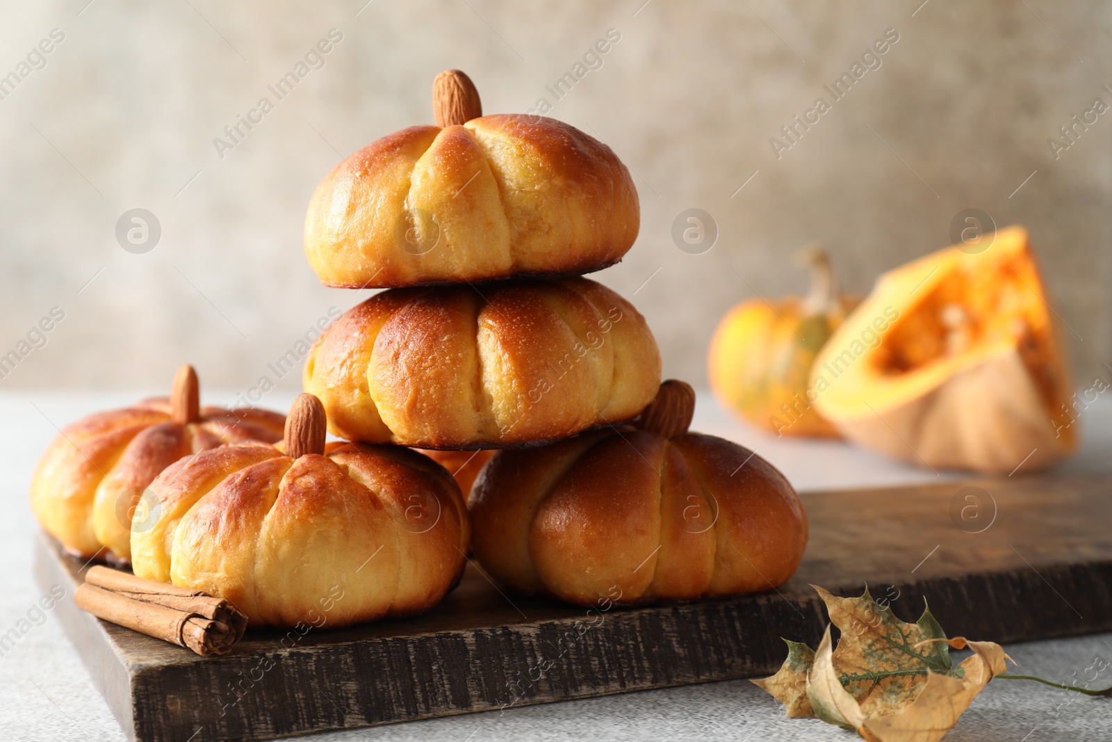 Photo of Tasty pumpkin shaped buns and cinnamon on light grey table, closeup