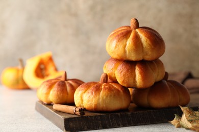 Photo of Tasty pumpkin shaped buns and cinnamon on light grey table, closeup