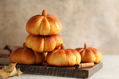 Photo of Tasty pumpkin shaped buns and cinnamon on light grey table, closeup