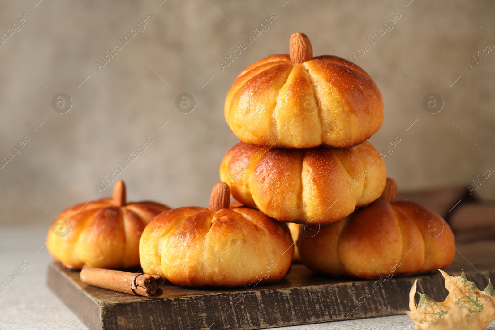 Photo of Tasty pumpkin shaped buns and cinnamon on light grey table, closeup