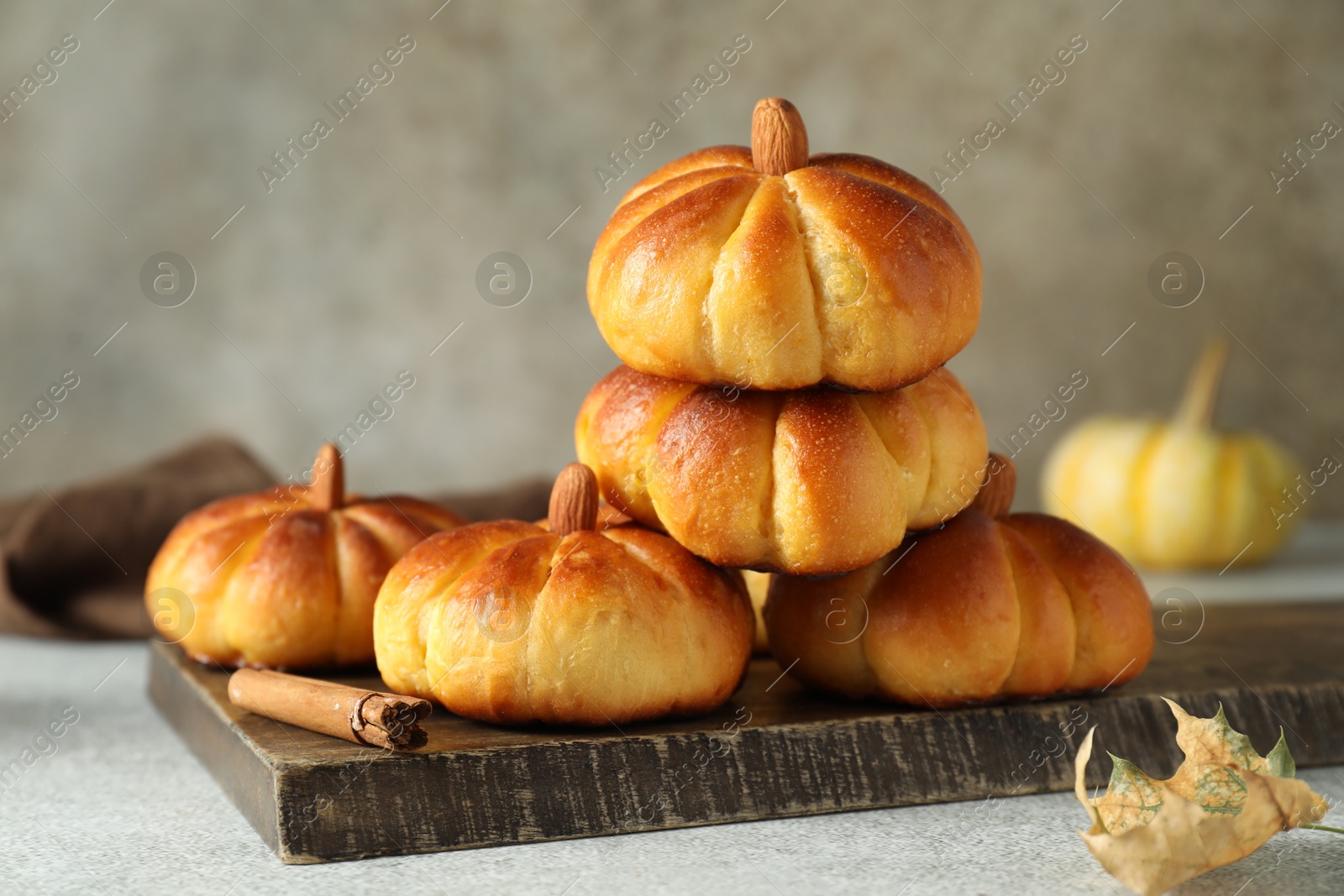 Photo of Tasty pumpkin shaped buns and cinnamon on light grey table, closeup