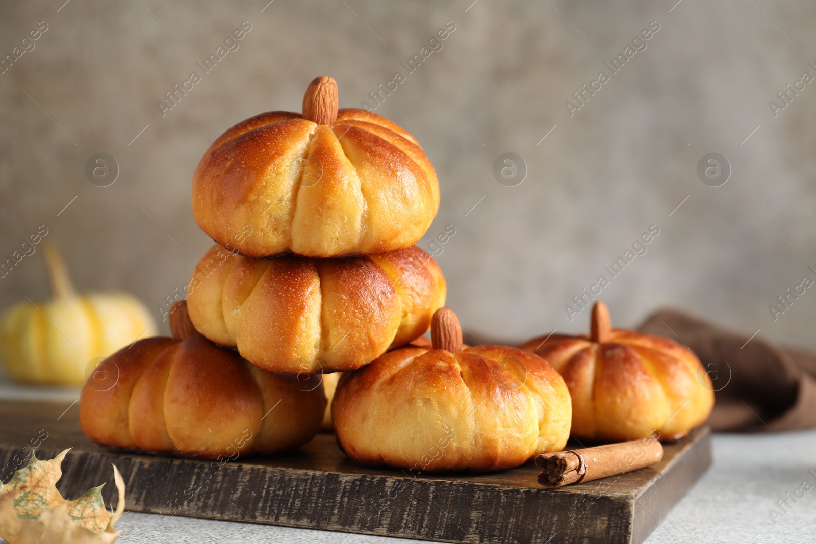 Photo of Tasty pumpkin shaped buns and cinnamon on light grey table, closeup