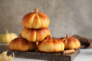 Photo of Tasty pumpkin shaped buns and cinnamon on light grey table, closeup