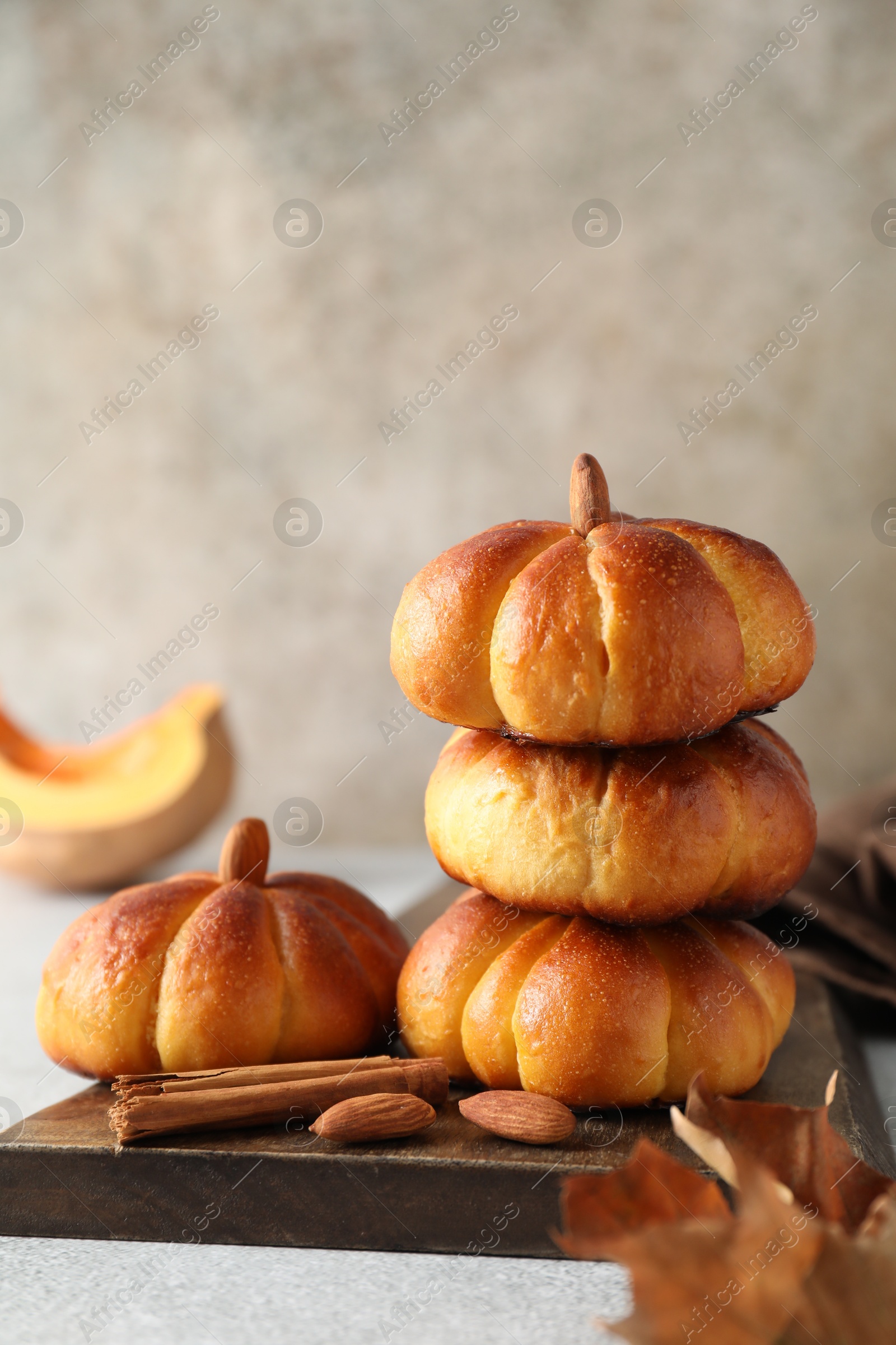 Photo of Tasty pumpkin shaped buns and cinnamon on light grey table, closeup