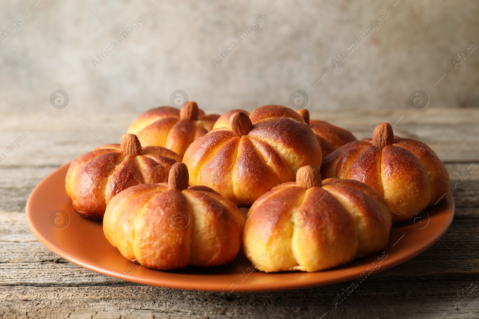 Photo of Tasty pumpkin shaped buns on wooden table, closeup