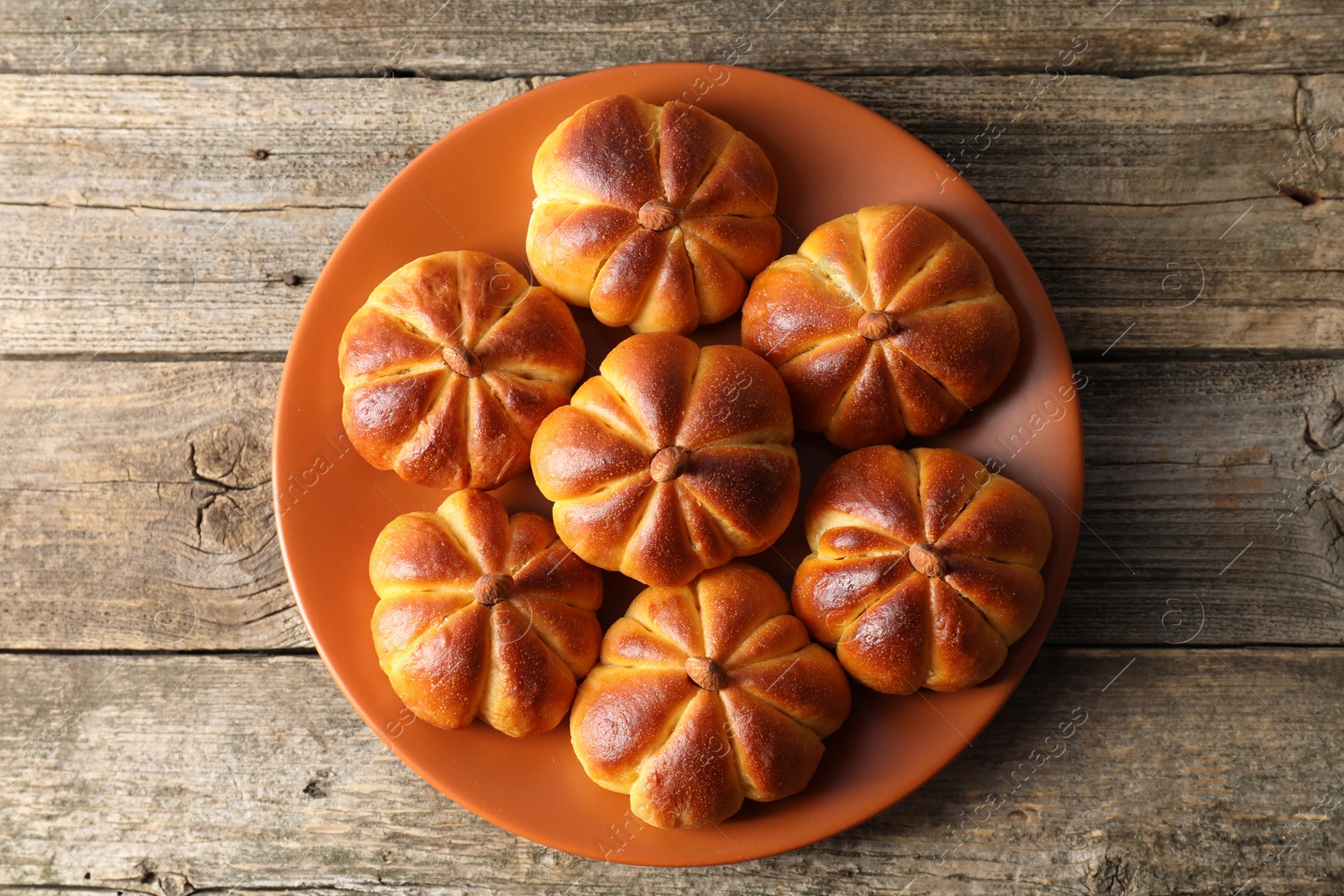 Photo of Tasty pumpkin shaped buns on wooden table, top view