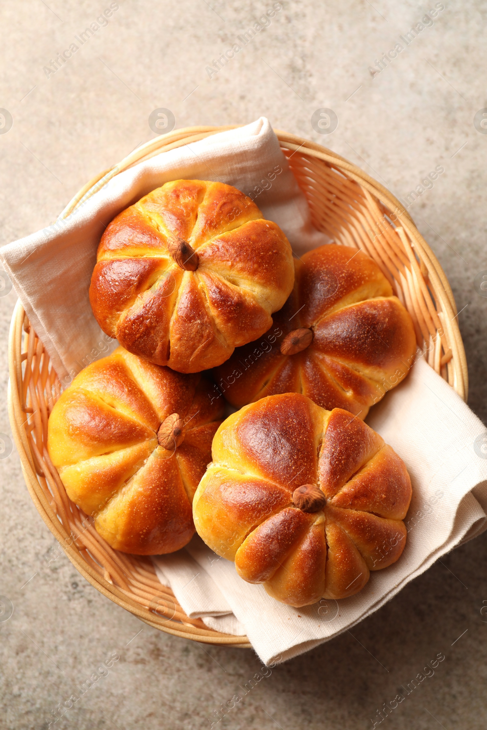 Photo of Tasty pumpkin shaped buns in wicker bowl on grey textured table, top view