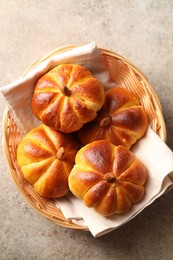 Photo of Tasty pumpkin shaped buns in wicker bowl on grey textured table, top view