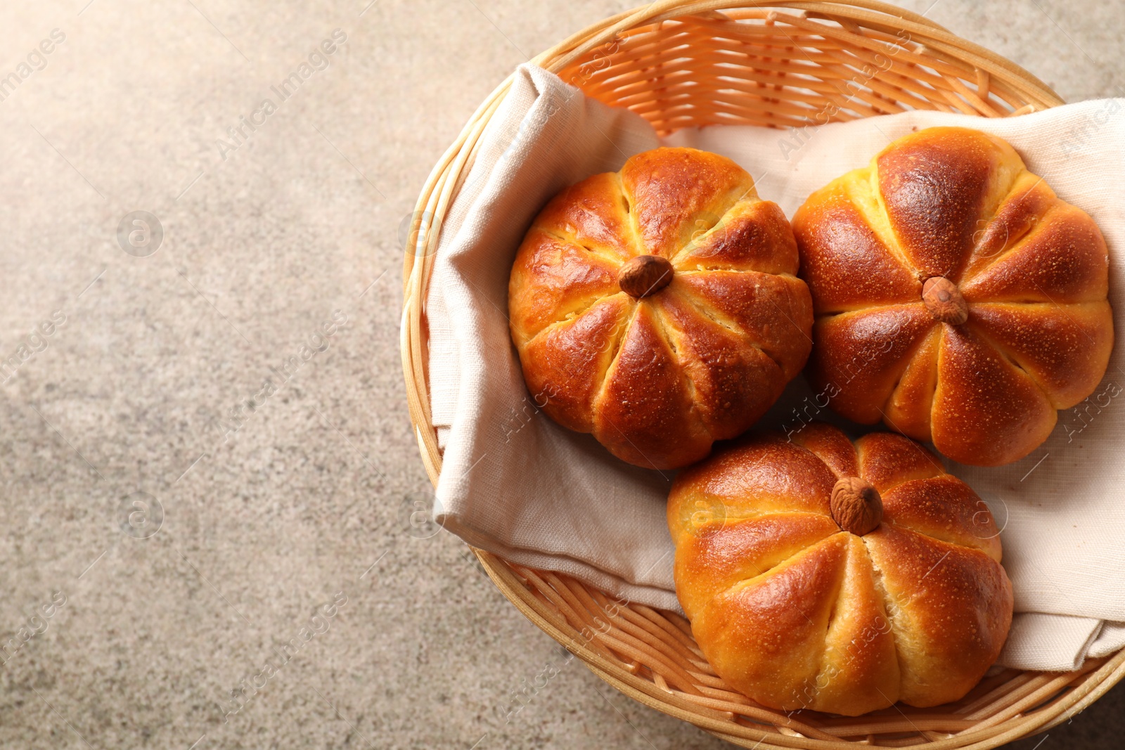 Photo of Tasty pumpkin shaped buns in wicker bowl on grey textured table, top view. Space for text