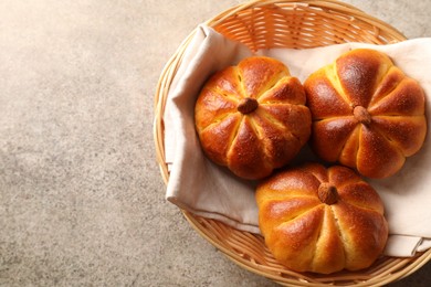 Photo of Tasty pumpkin shaped buns in wicker bowl on grey textured table, top view. Space for text