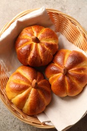 Photo of Tasty pumpkin shaped buns in wicker bowl on grey textured table, top view