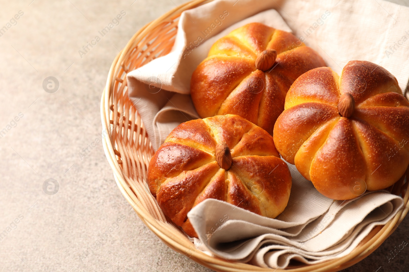 Photo of Tasty pumpkin shaped buns in wicker bowl on grey textured table, closeup