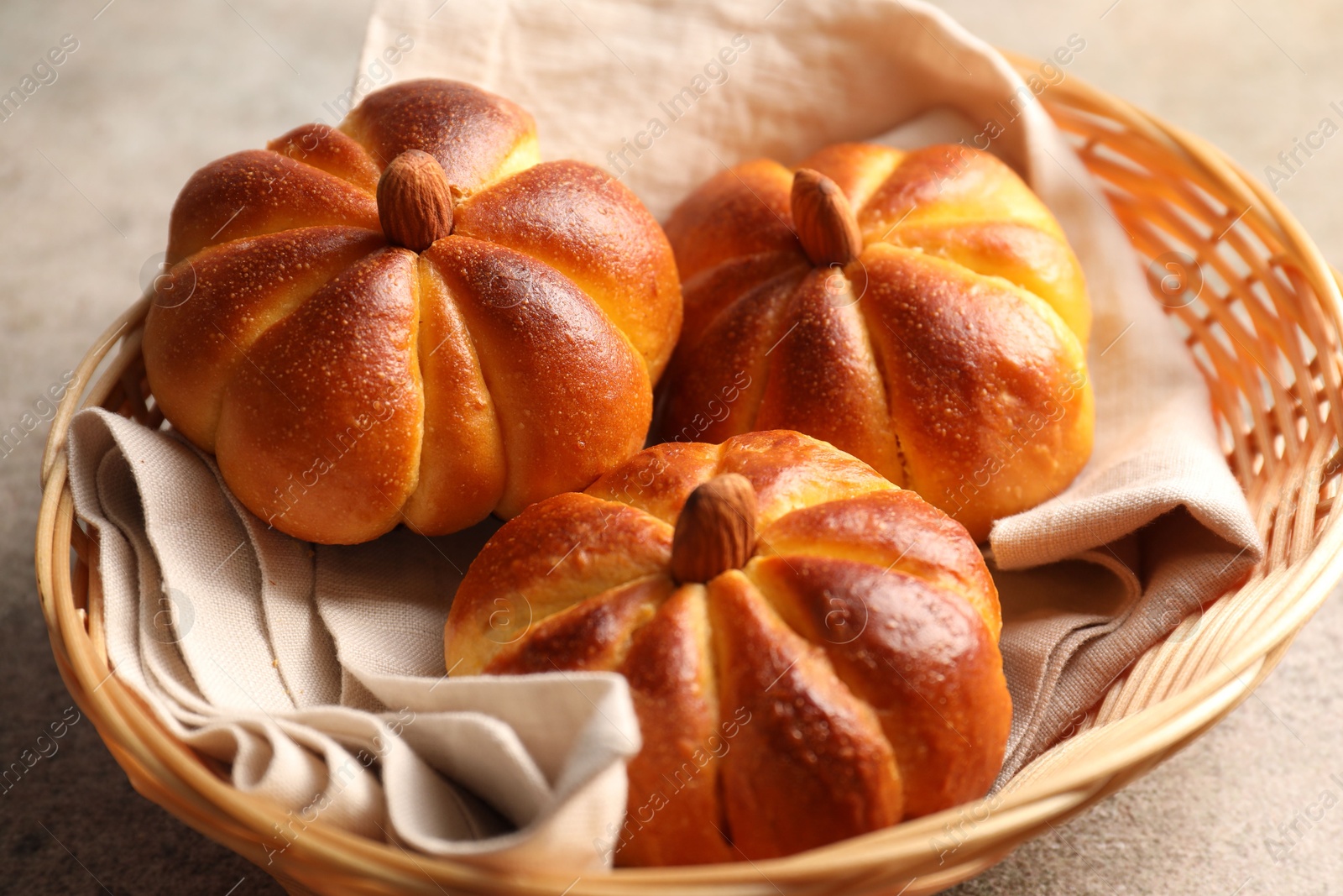 Photo of Tasty pumpkin shaped buns in wicker bowl on grey textured table, closeup