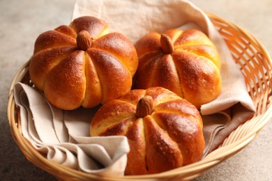 Photo of Tasty pumpkin shaped buns in wicker bowl on grey textured table, closeup