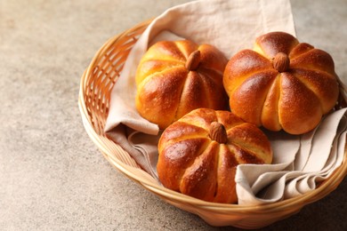 Photo of Tasty pumpkin shaped buns in wicker bowl on grey textured table, closeup