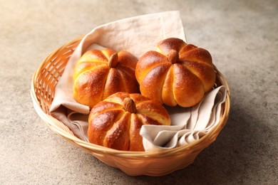 Photo of Tasty pumpkin shaped buns in wicker bowl on grey textured table, closeup