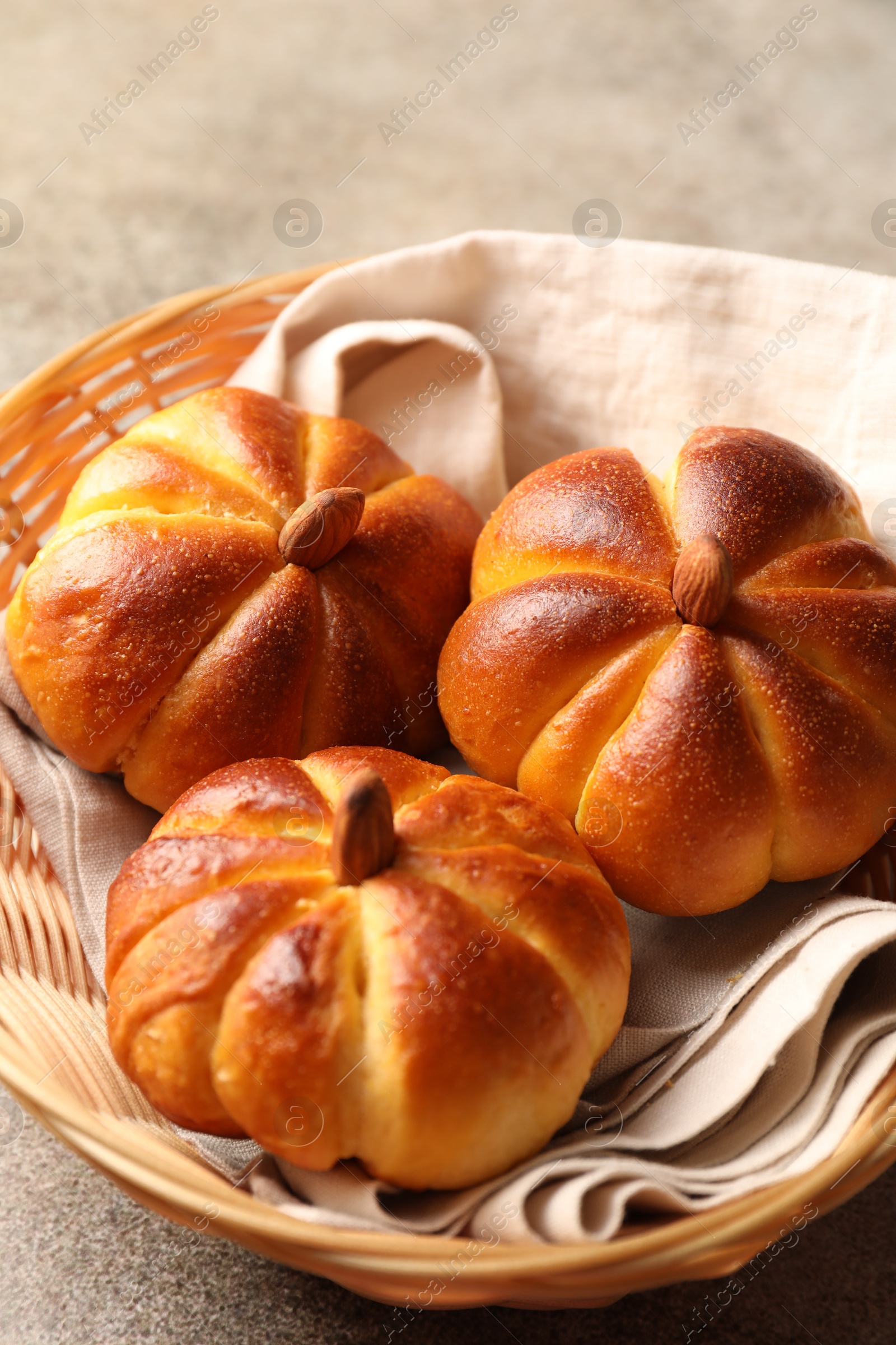 Photo of Tasty pumpkin shaped buns in wicker bowl on grey textured table, closeup