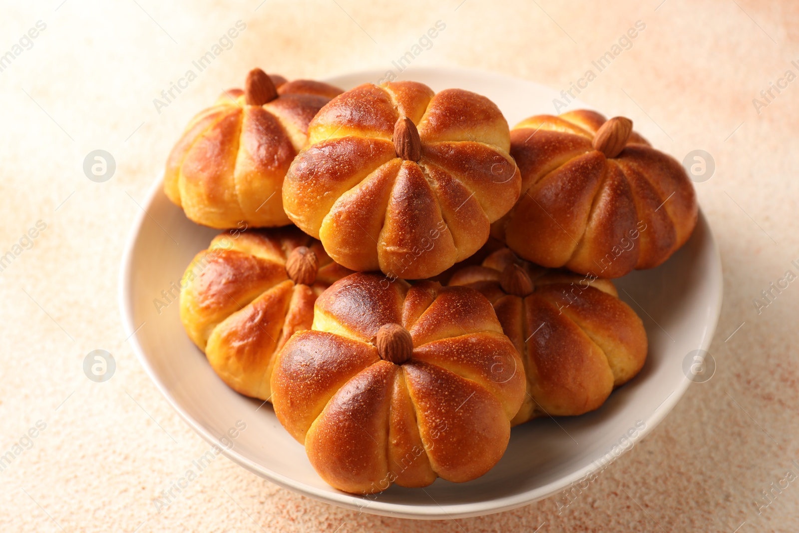 Photo of Tasty pumpkin shaped buns on beige textured table, closeup