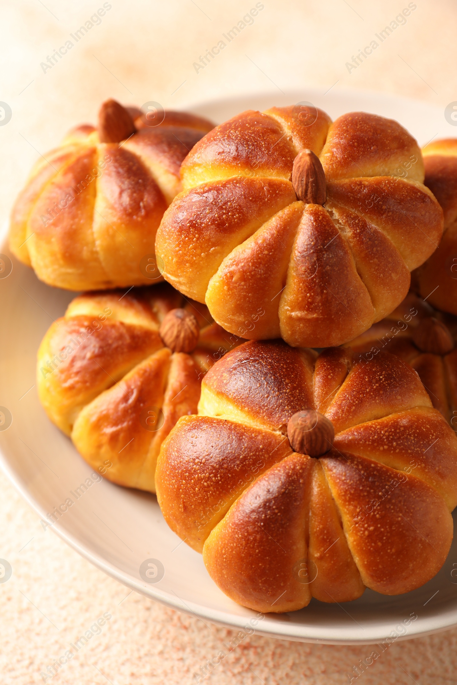 Photo of Tasty pumpkin shaped buns on beige textured table, closeup