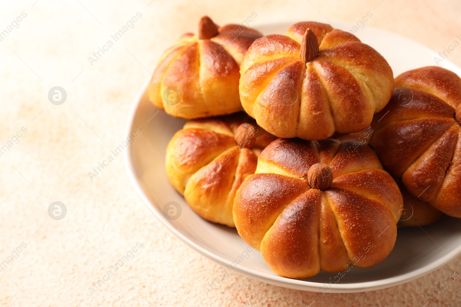 Photo of Tasty pumpkin shaped buns on beige textured table, closeup