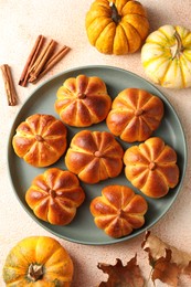 Photo of Tasty pumpkin shaped buns, ingredients and dry leaves on beige textured table, flat lay